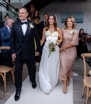 Father of the bride walking his daughter down the aisle in a black peak lapel tuxedo.